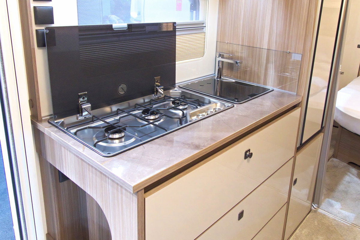 2026 Caravan Salon'da Fendt Tendenza 560 SFDW: 3 gözlü ocak, lavabo, buzdolabı ve depolama alanı içeren mutfak bölümü.